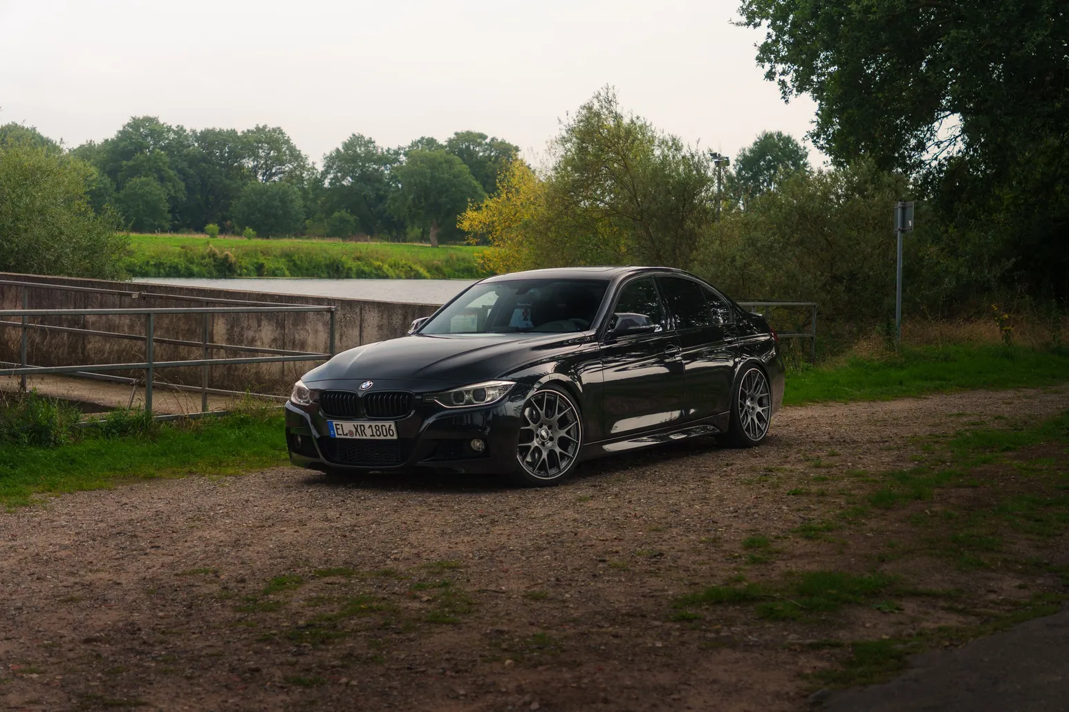 Black BMW F30 3 Series on a gravel lot with trees behind