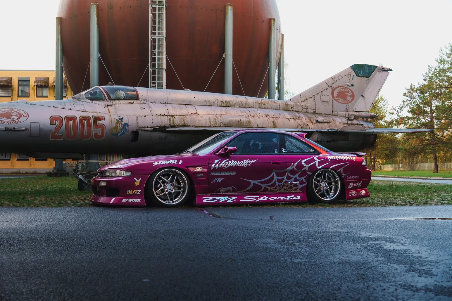 Pinker Nissan Silvia S14 Drift-Wagen neben einem ausgemusterten MiG-Kampfjet