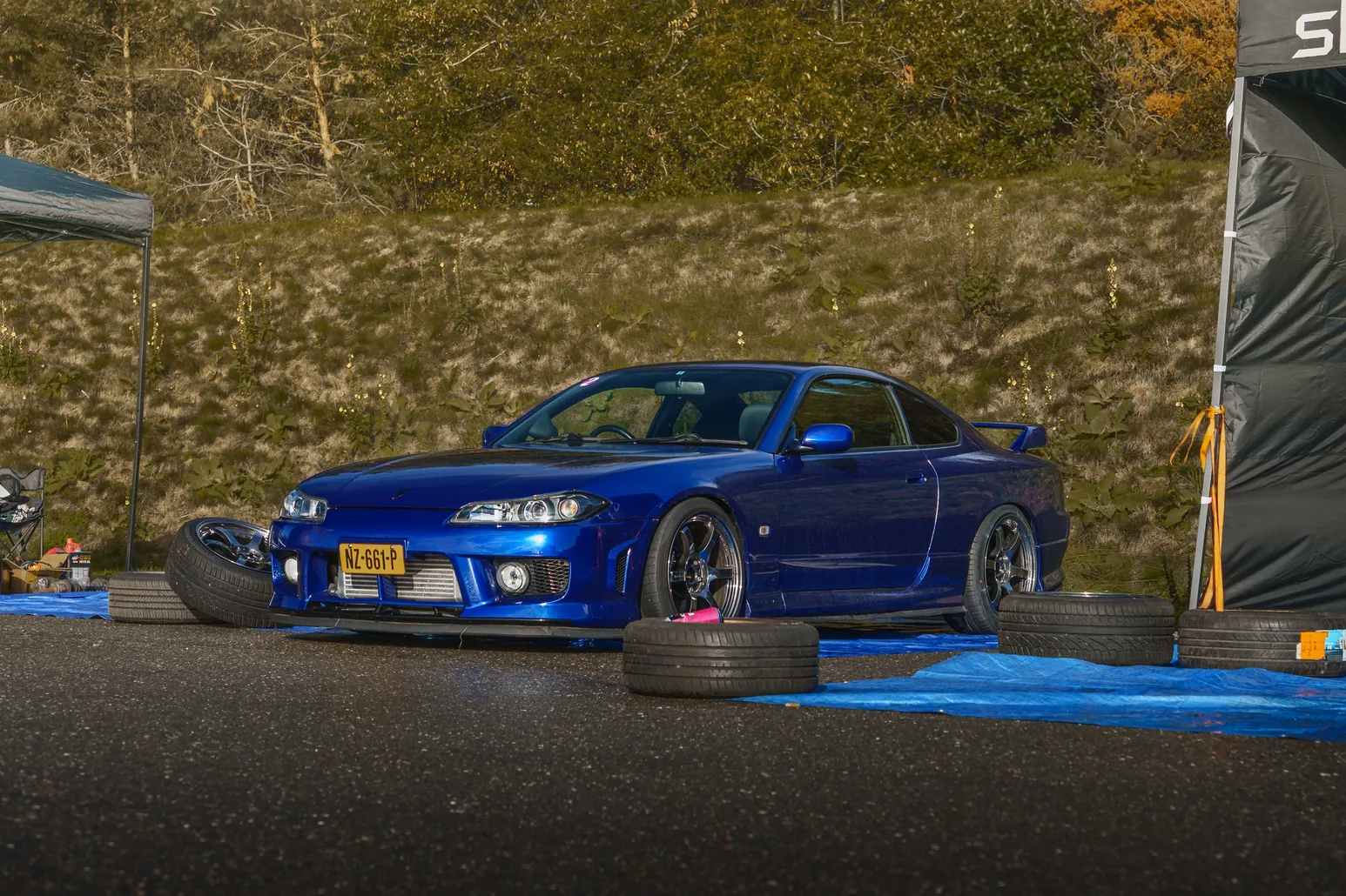 Blauer Nissan Silvia S15 mit Ersatzreifen neben einem Boxenzelt