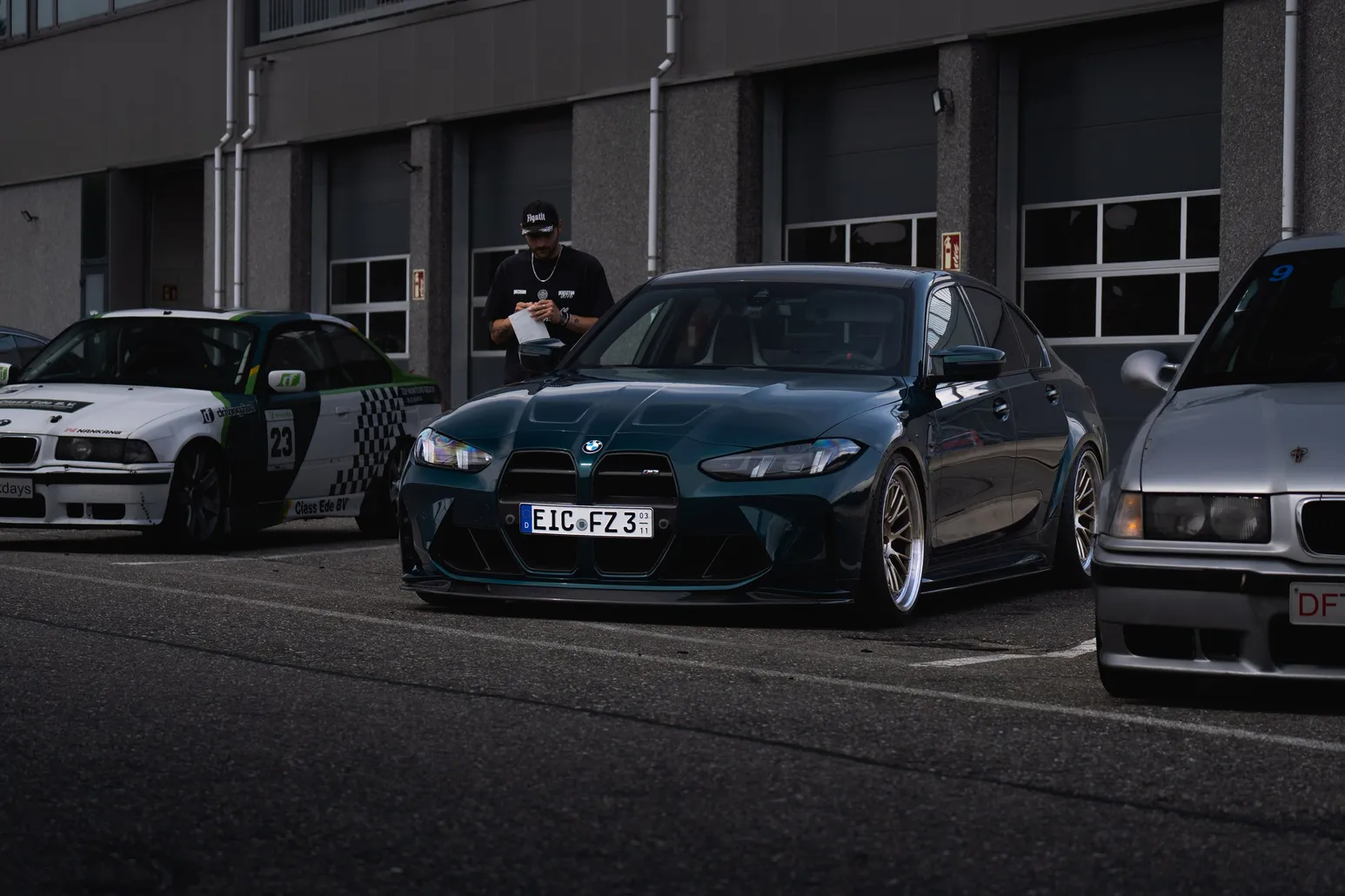 Green BMW M3 with people and cars at the pit garages