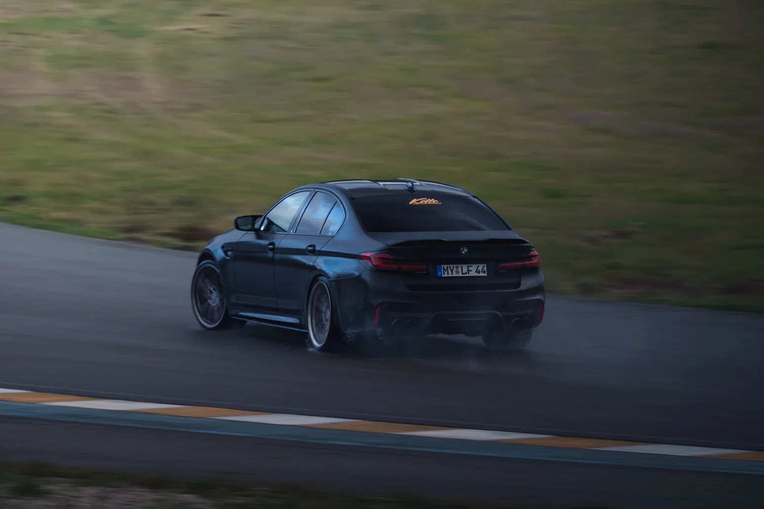 Black BMW M5 (F90) from the rear three-quarter on the wet track