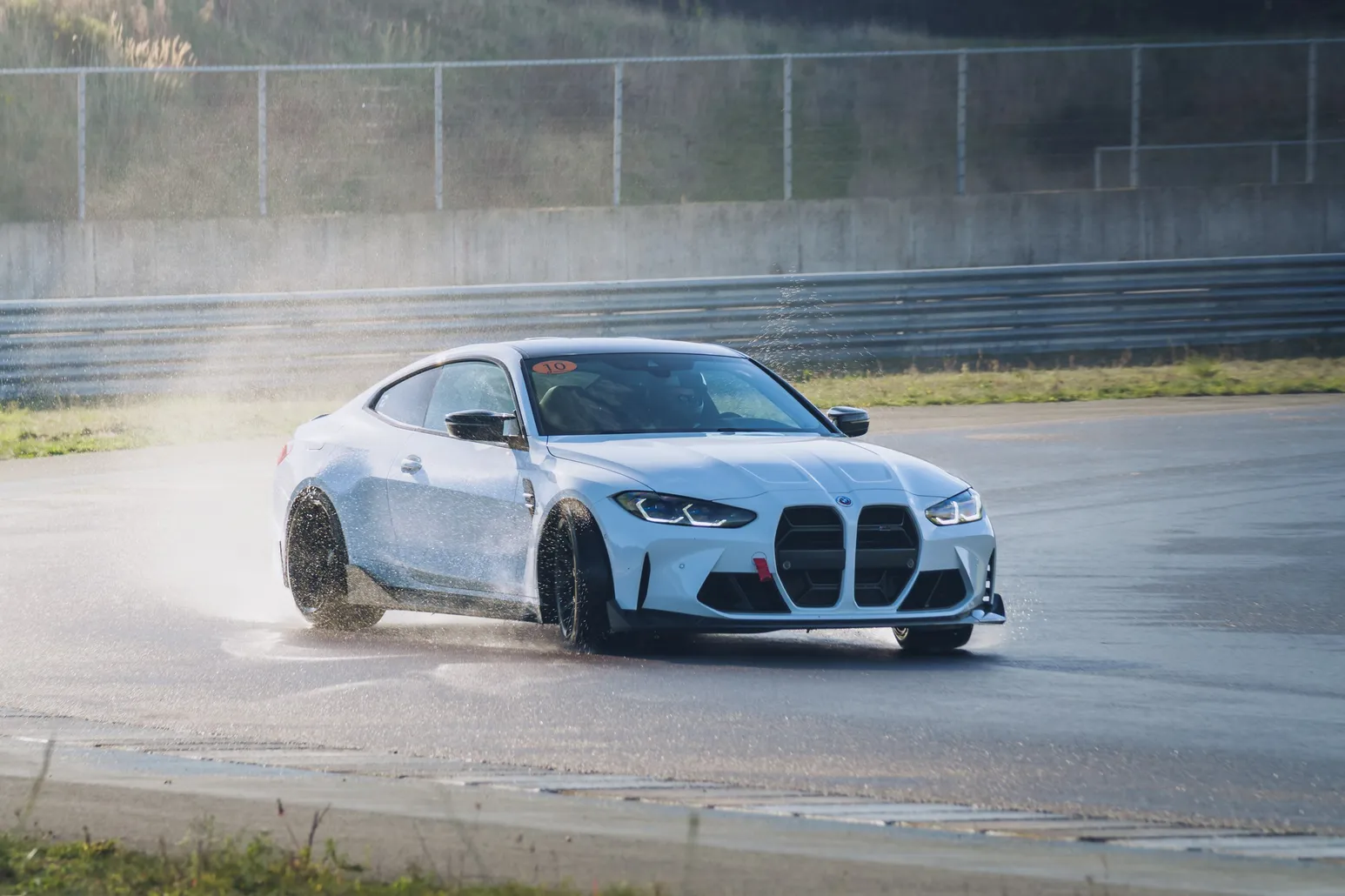 White BMW M4 (G82) drifting head-on through the spray of the wet track