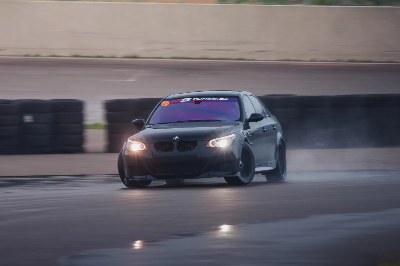 Black BMW M5 (E60) with headlights on a reflective wet surface
