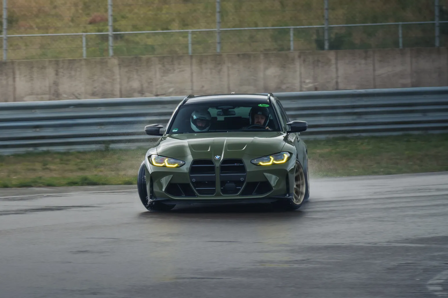 Olive green BMW M3 Touring head-on with headlights on