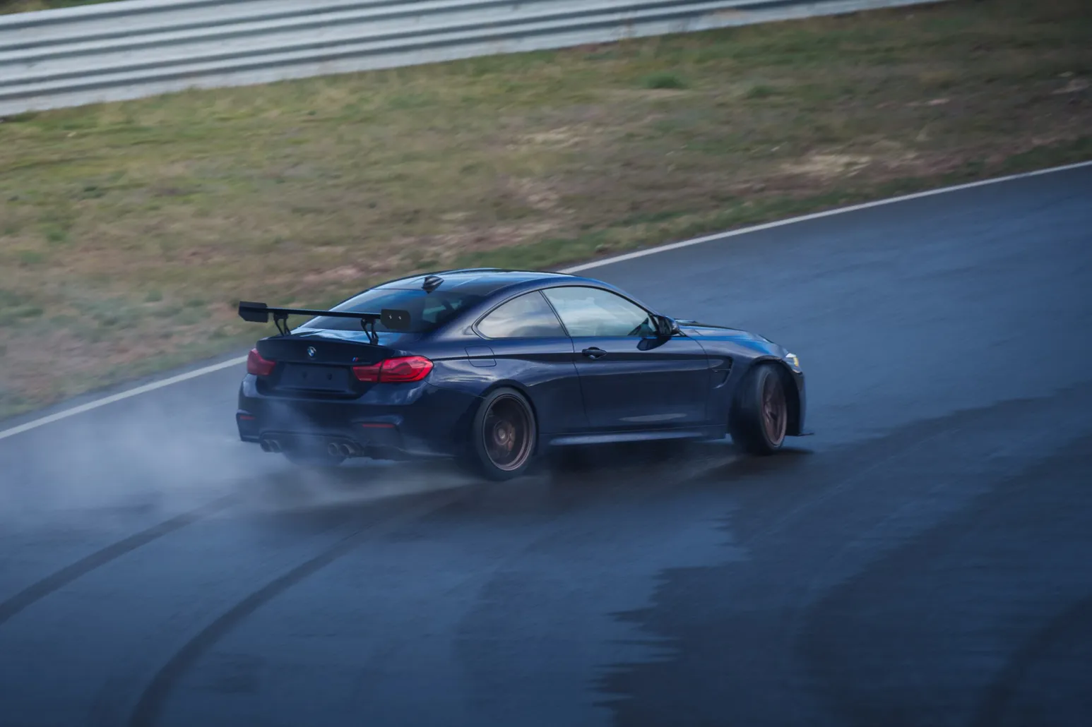 Dark blue BMW M4 with rear wing drifting on the wet track