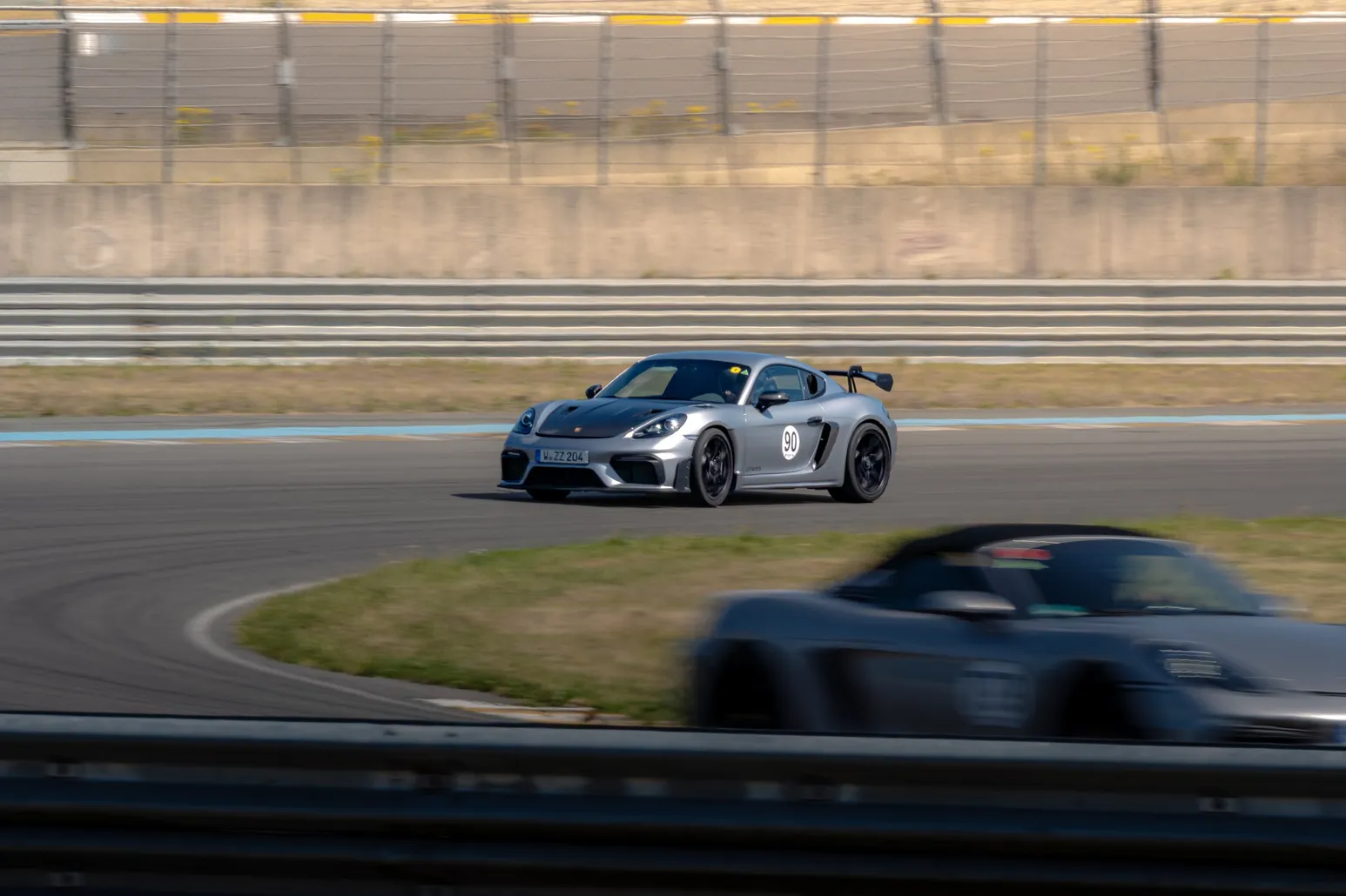 Silberner Porsche Cayman GT4, im Vordergrund unscharf ein Boxster