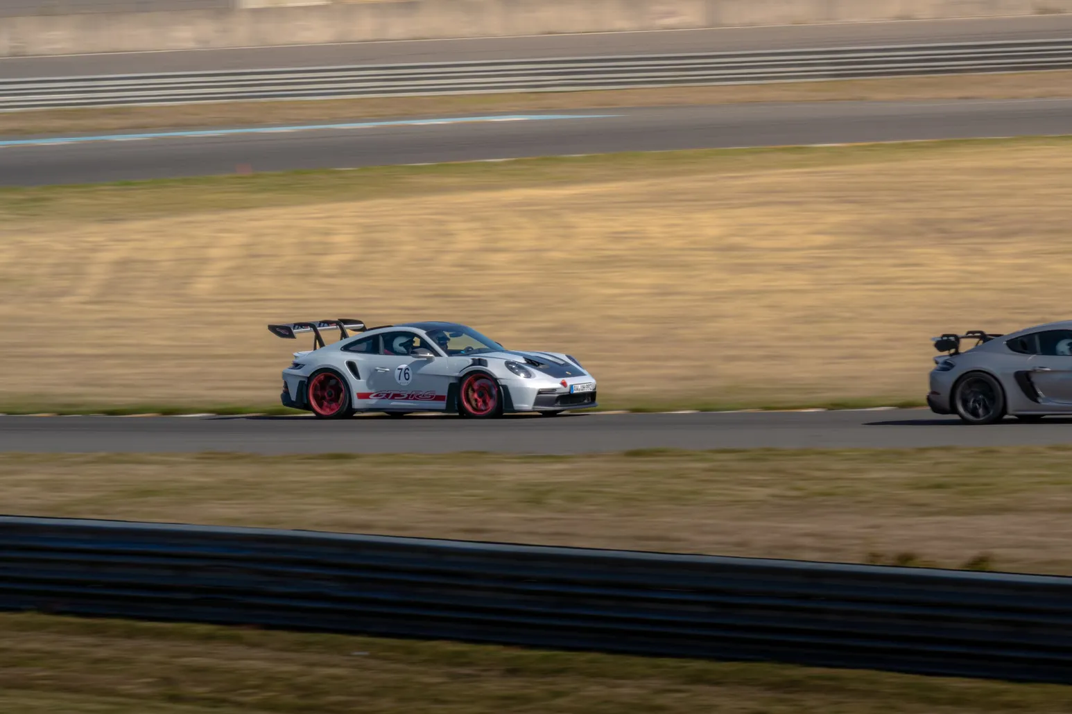 Porsche 911 GT3 RS als weiter Mitzieher vor trockenem Gras