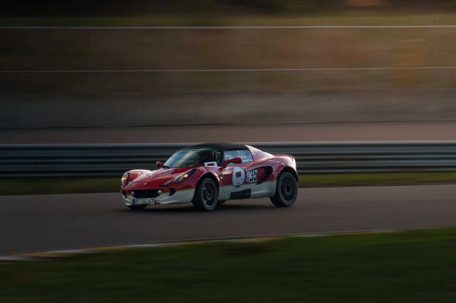 Red and white Lotus Elise in race trim, panning shot on track
