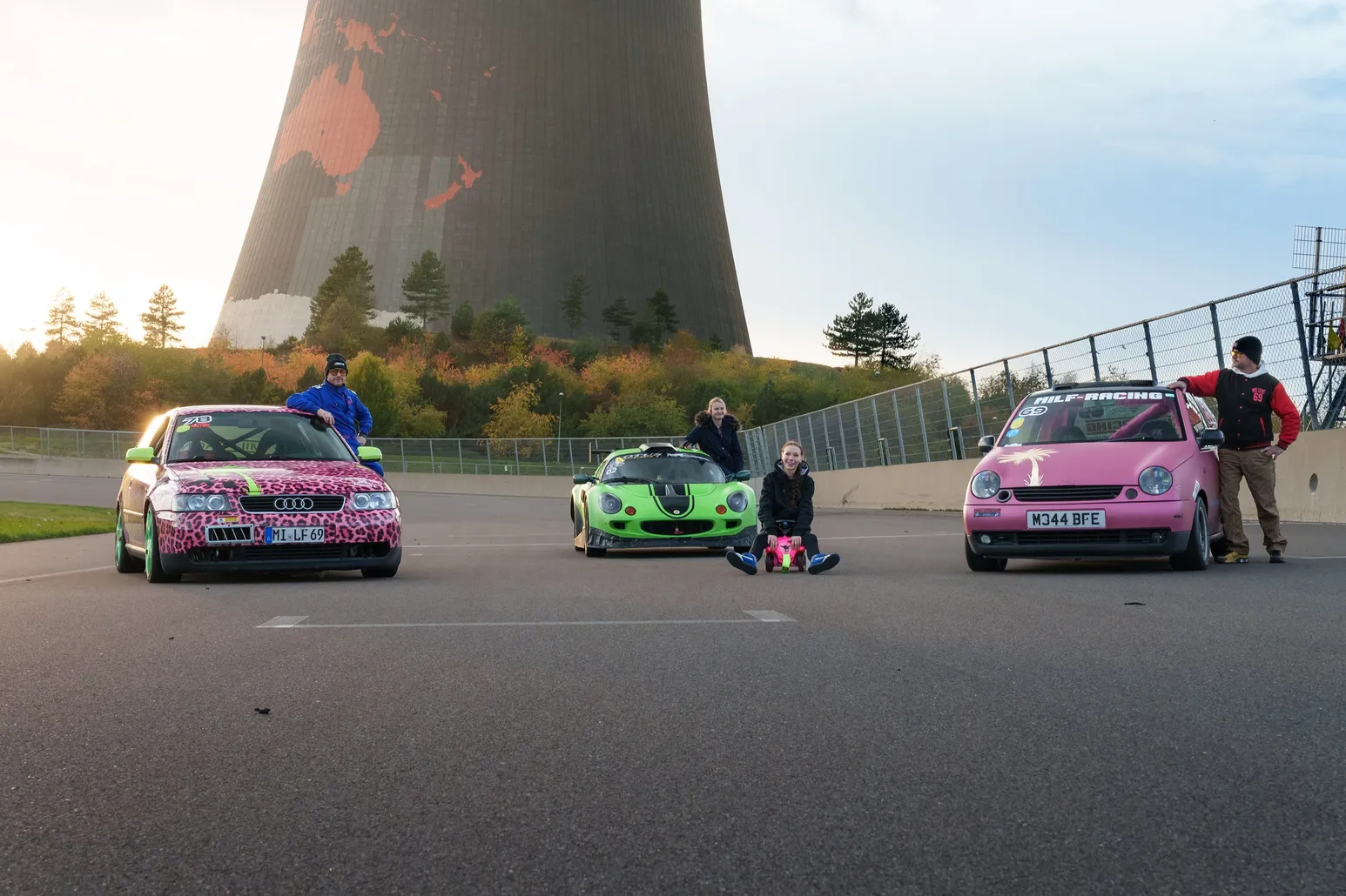 Team with a pink Audi A3, green Lotus Elise and pink Lupo in front of the painted cooling tower