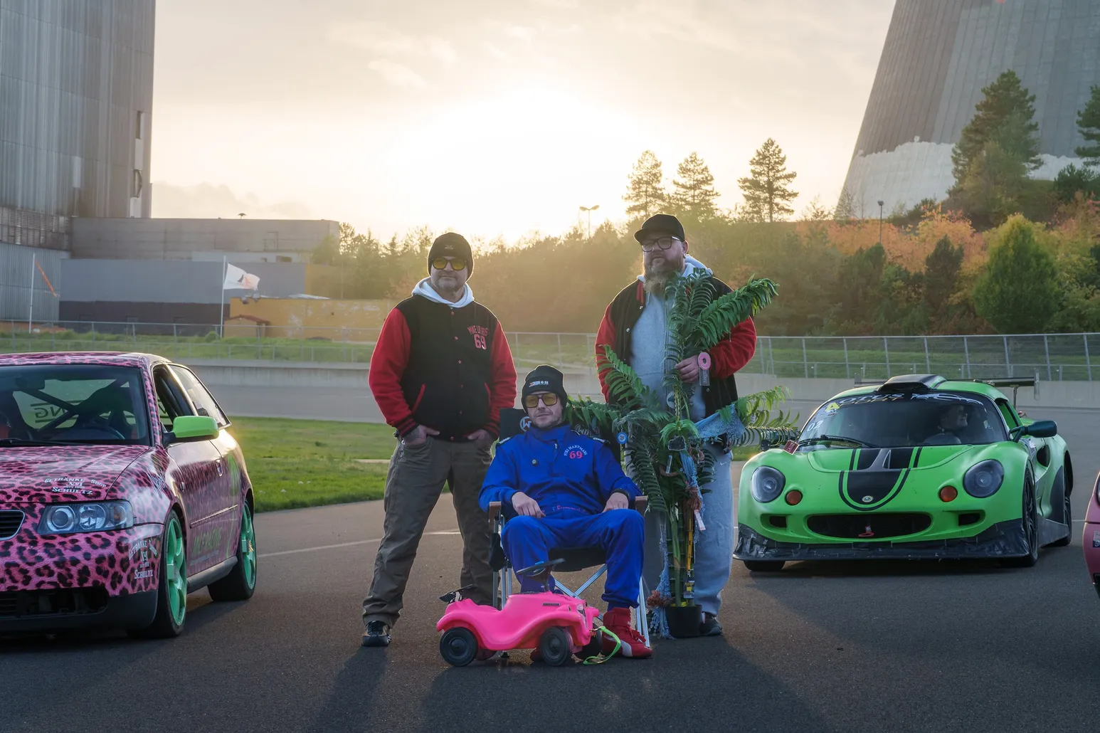 Team group photo with a pink ride-on toy car between the cars