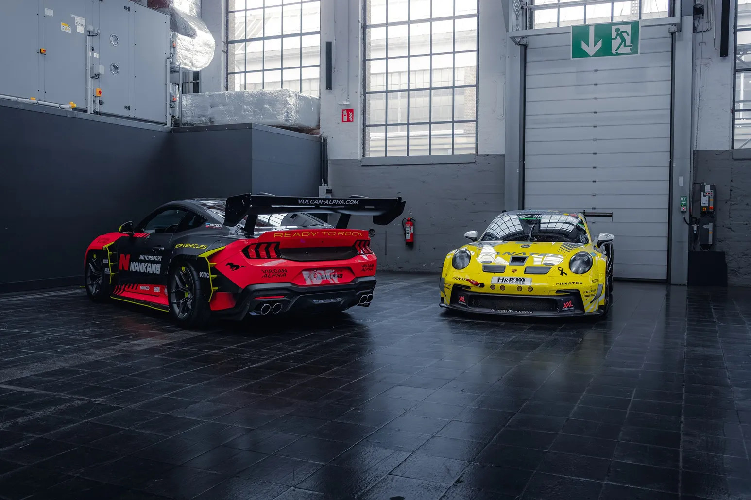 Race car with a large rear wing next to a yellow Porsche