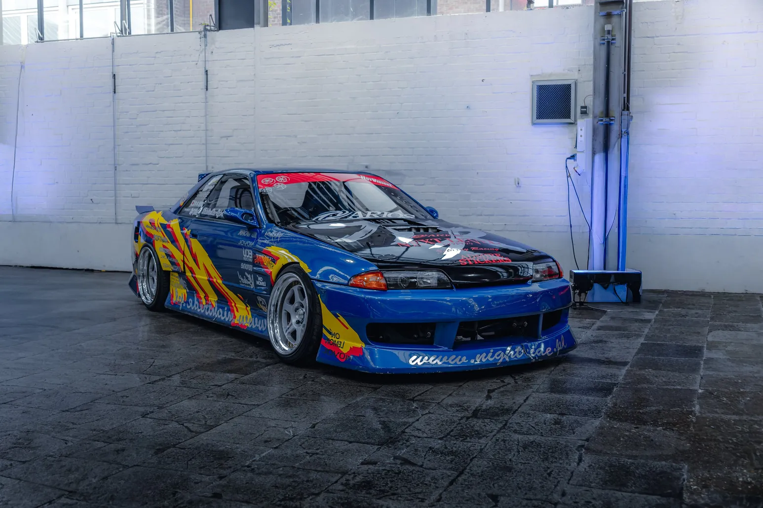 Nissan Skyline R32 with colourful race livery against a white wall