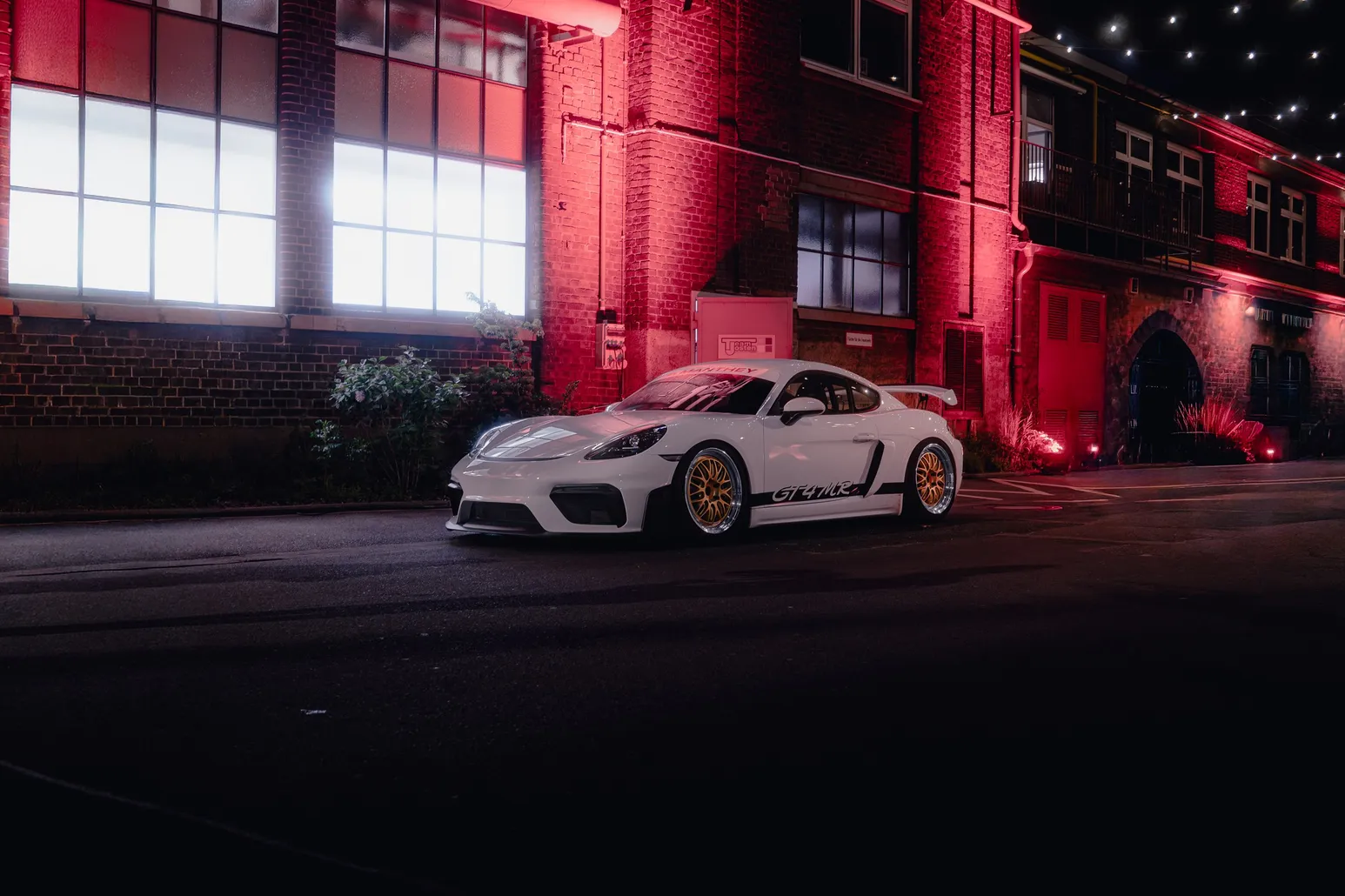 White Porsche Cayman GT4 RS in front of a red-lit brick facade