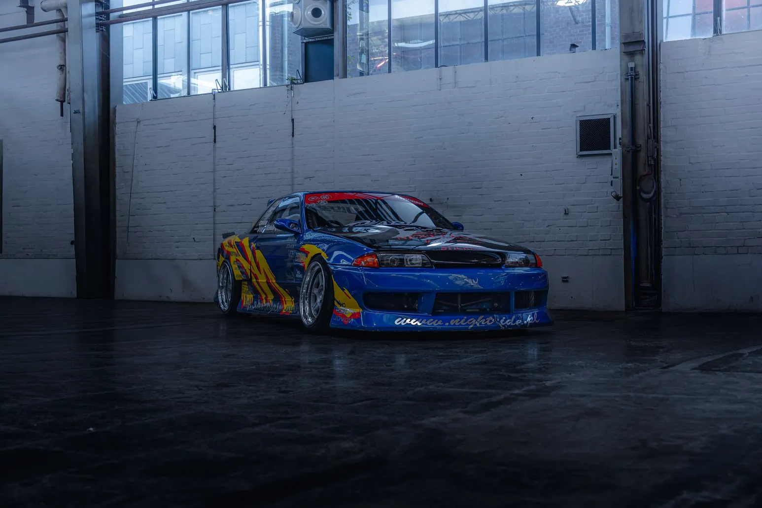 Nissan Skyline R32 with race livery against a white hall wall