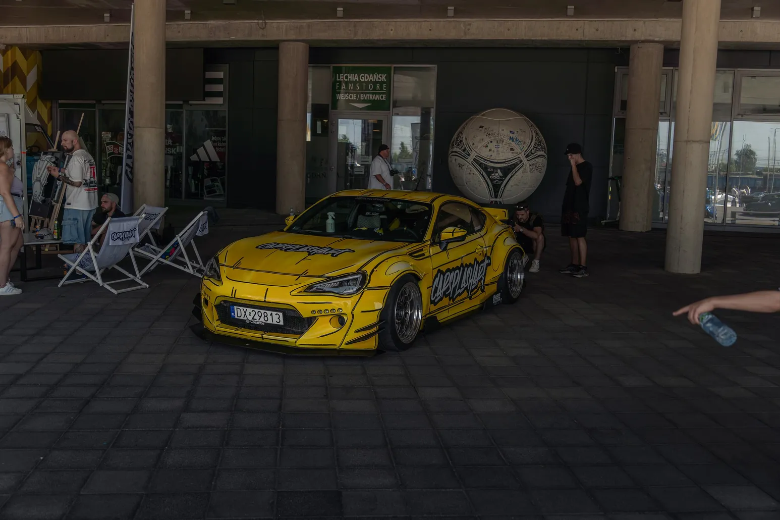 Yellow widebody Toyota GT86 under the stadium canopy