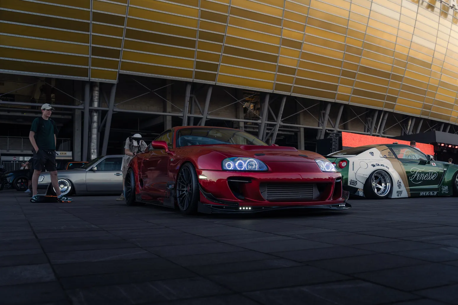 Red widebody Toyota Supra in front of the golden stadium