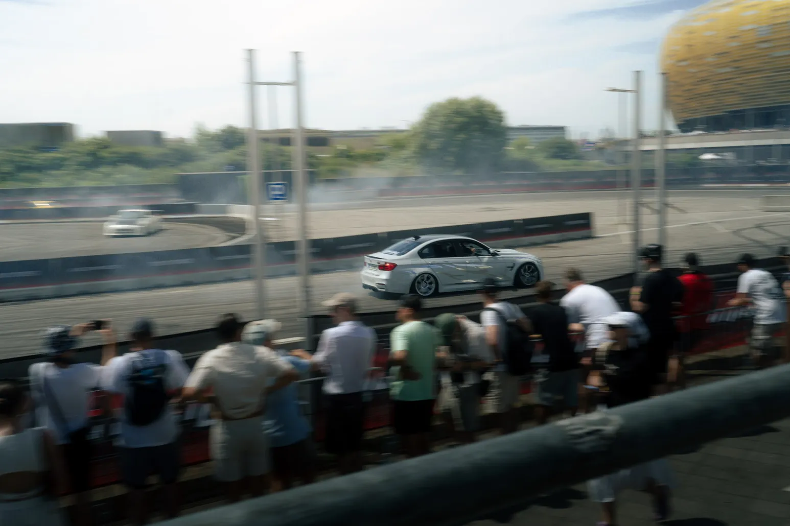White BMW drifting with spectators and stadium behind