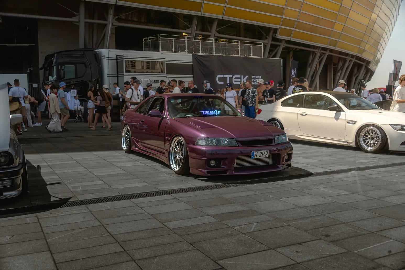 Purple Nissan Skyline next to a white BMW in front of the stadium