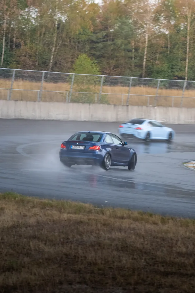 Black BMW drifting with a white car following, portrait format
