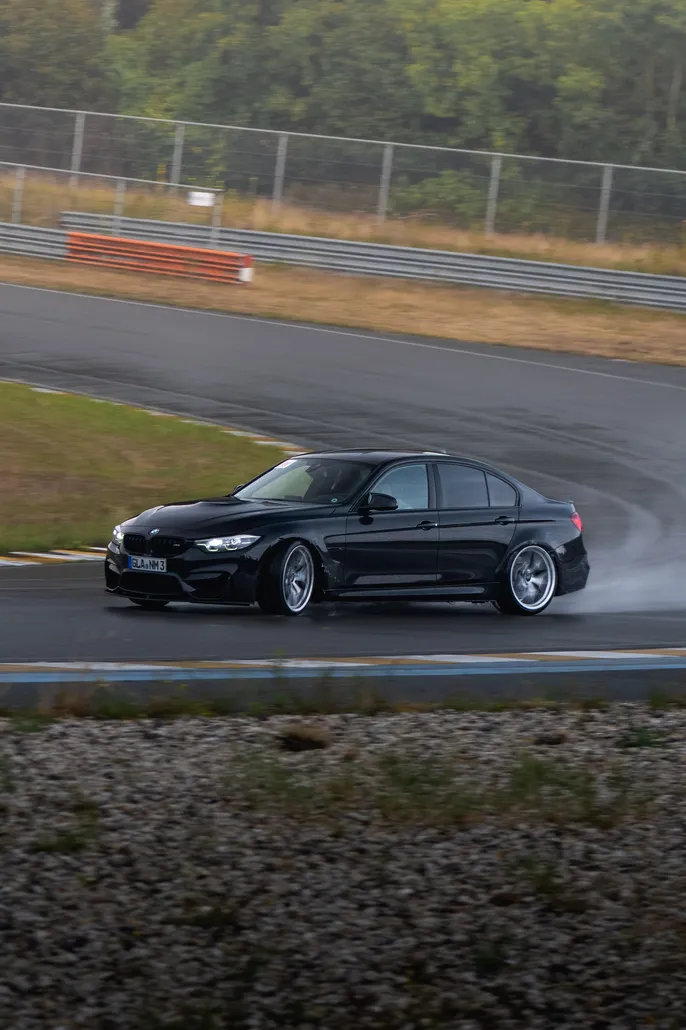 Black BMW M3 sliding through a wet bend
