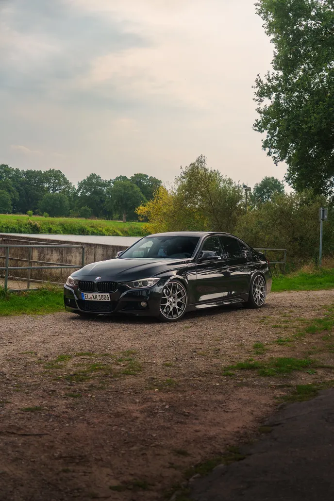 Black BMW F30 by a riverside wall, portrait format