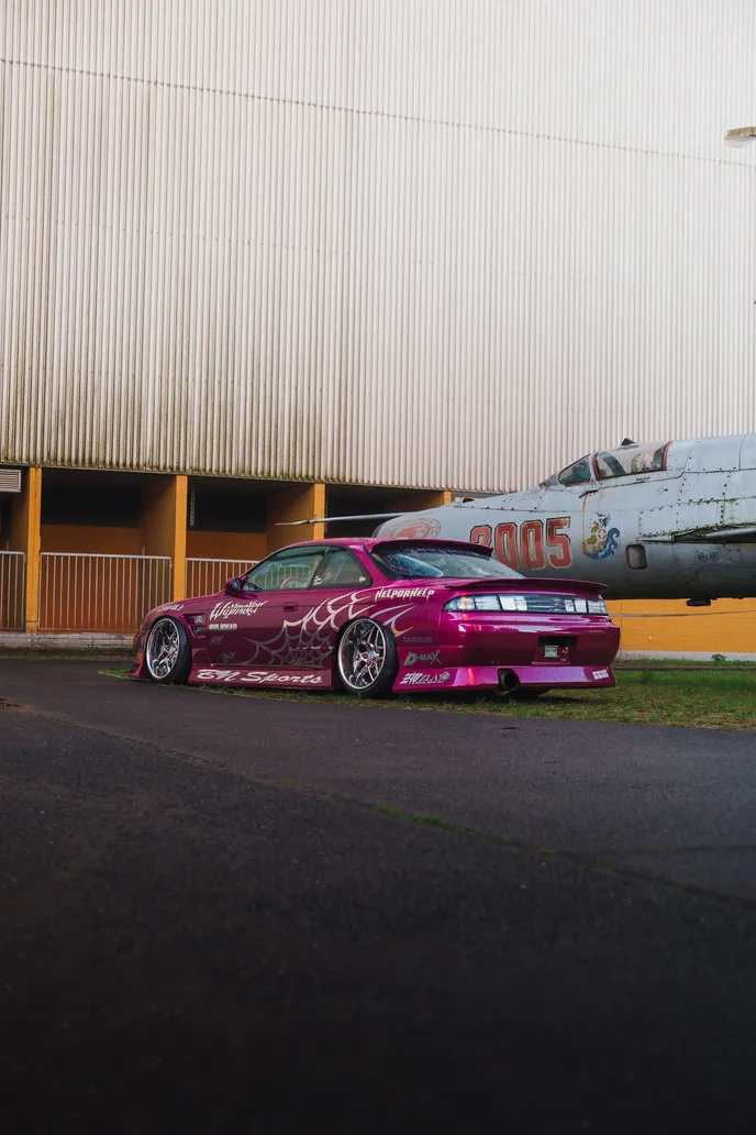 Pinker Silvia und MiG-Jet vor einer Wellblechwand