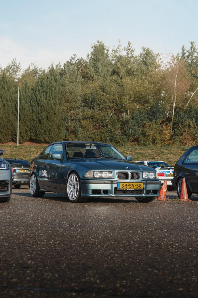 Grauer BMW E36 im Fahrerlager vor Bäumen