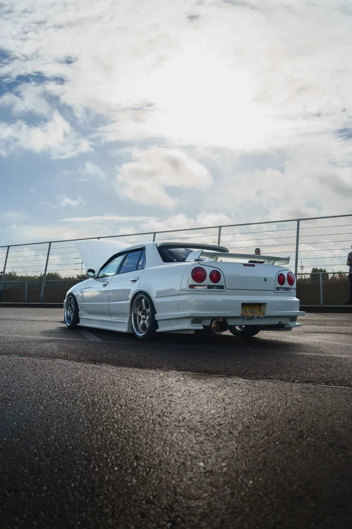 Weißer Nissan Skyline R34 von hinten unter hellem Himmel