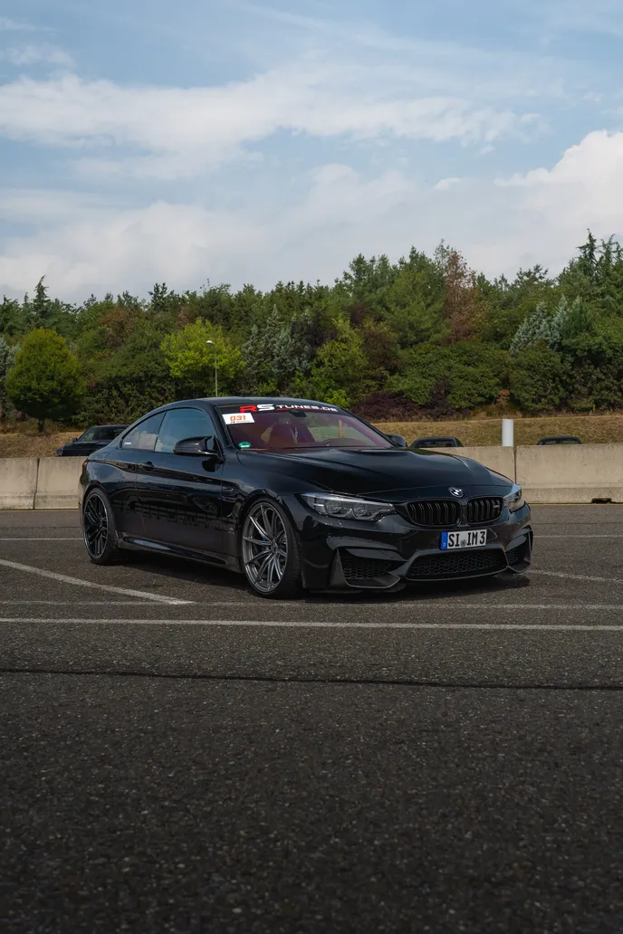 Black BMW M4 parked in the paddock, portrait format