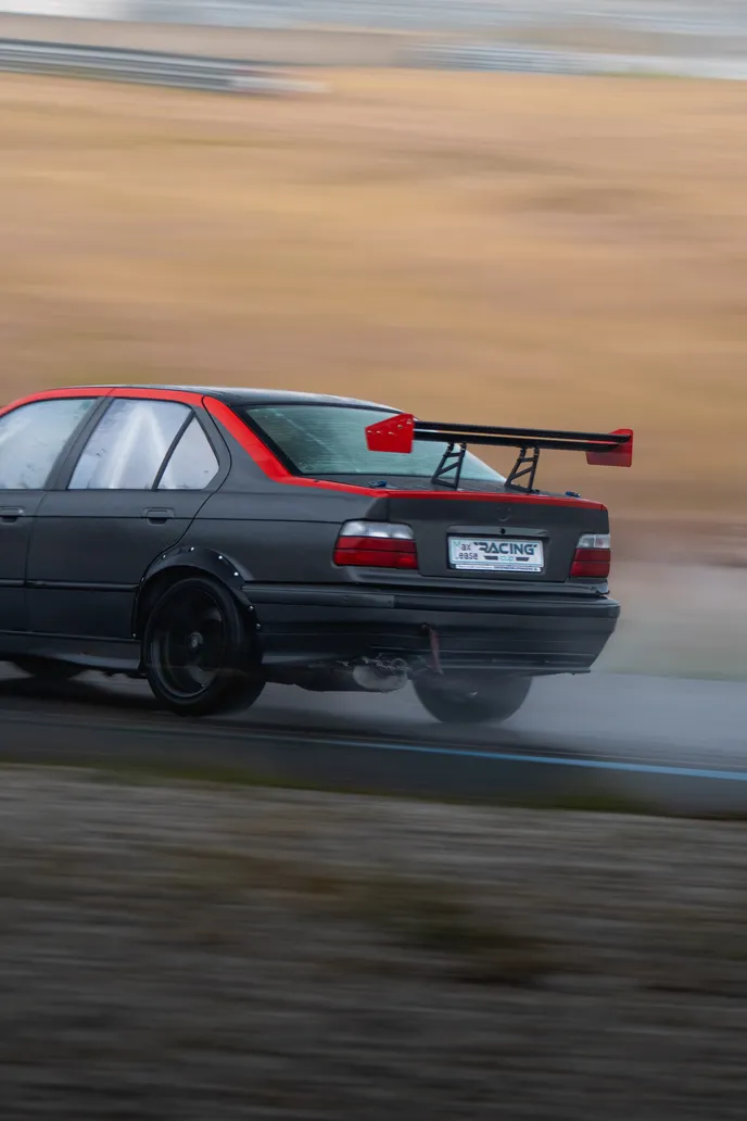 Grey BMW E36 with big rear wing sliding past