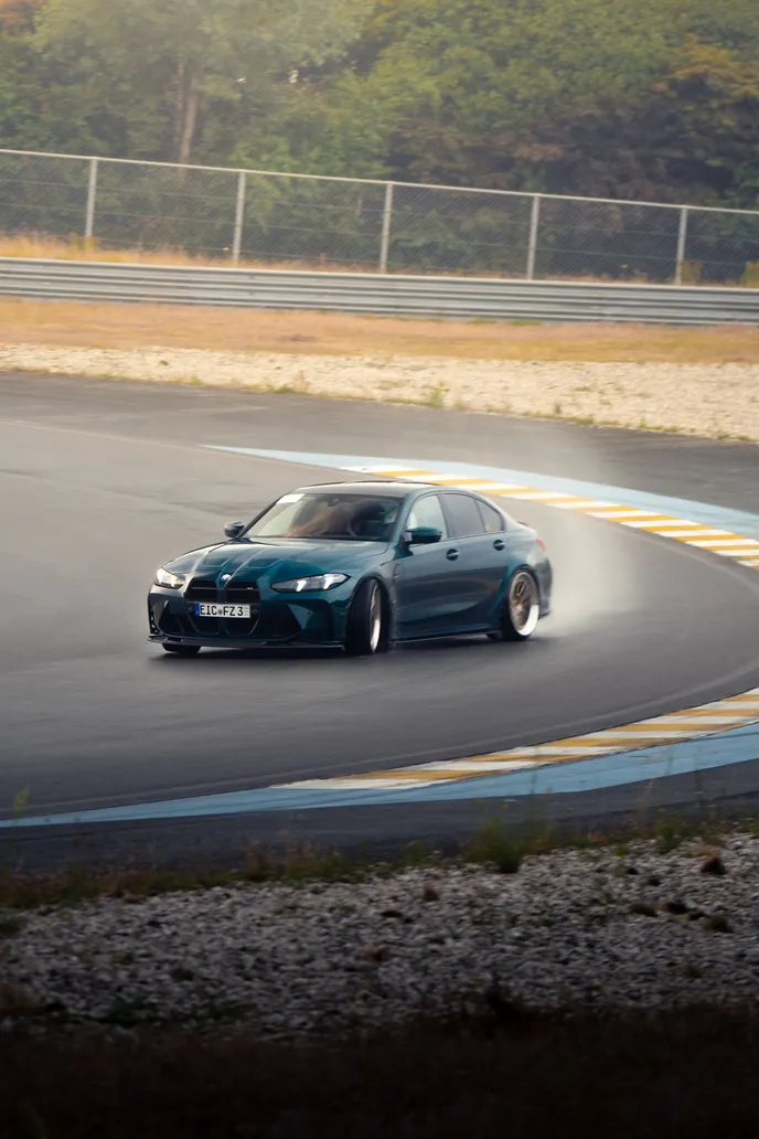 Green BMW M3 drifting over the blue and yellow kerb