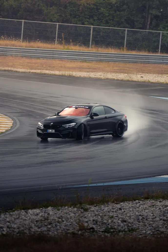 Black BMW M4 with orange interior drifting on wet tarmac