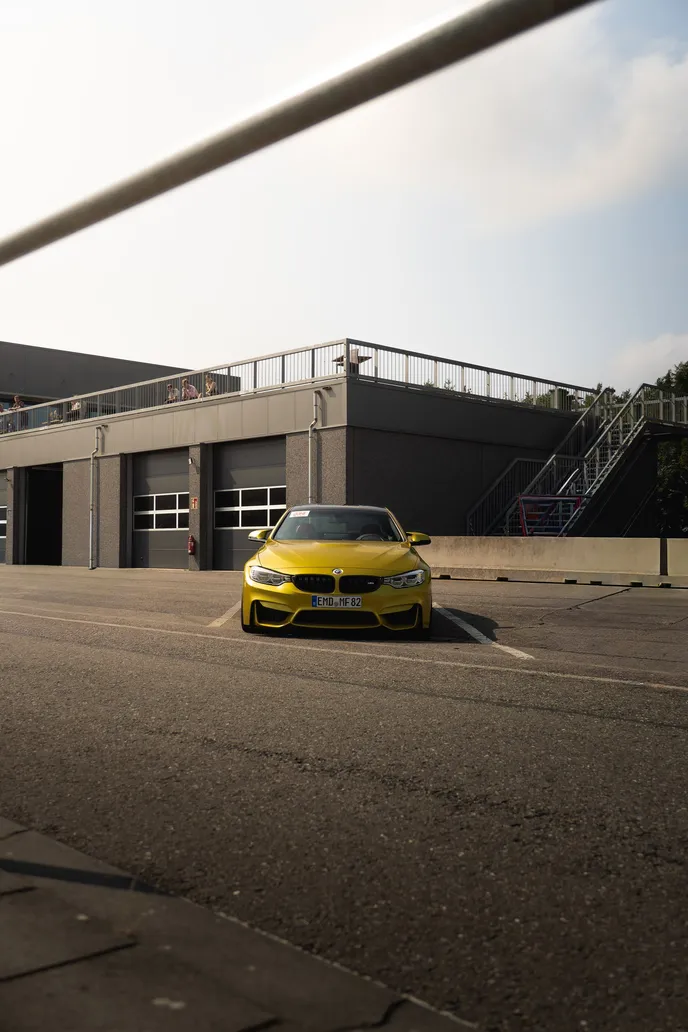 Yellow BMW M4 in front of the pit building, portrait format