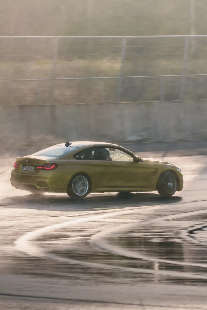 Gelber BMW M4 rutscht auf nassem Asphalt, Hochformat