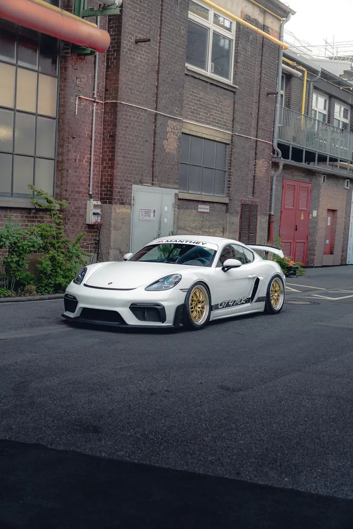 White Porsche Cayman GT4 RS in front of a brick facade, portrait format