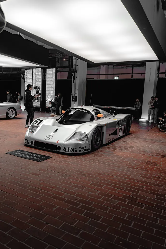 Silver Group C race car under a light panel, portrait format