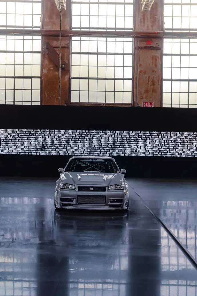 Silver Nissan Skyline head-on in front of a light installation, portrait format