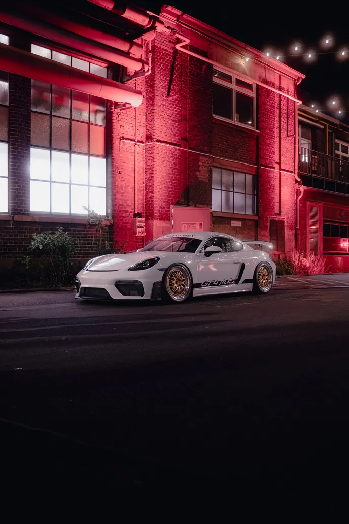Porsche Cayman GT4 RS in front of the red facade at night, portrait format