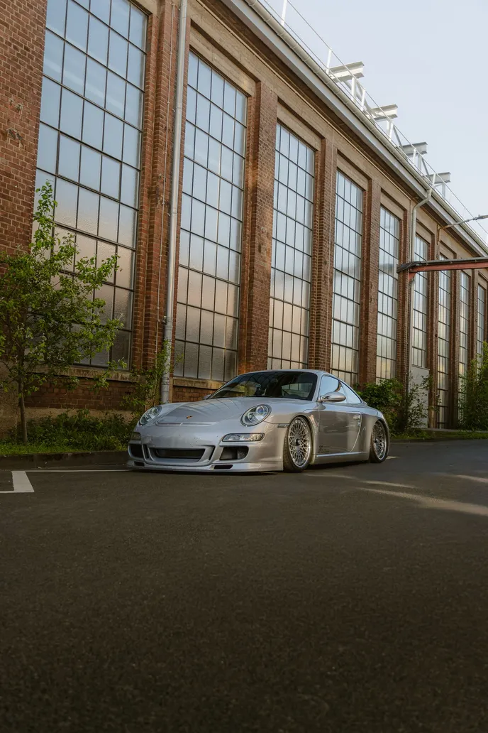 Silver Porsche 911 in front of large factory windows, portrait format