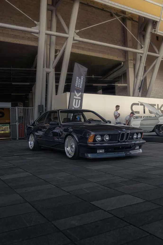 Black BMW E24 at the stadium entrance, portrait format