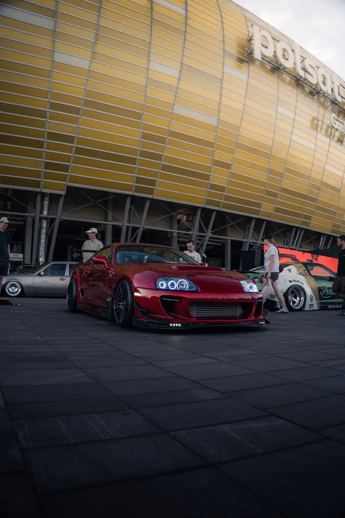 Red Toyota Supra in front of the stadium facade, portrait format